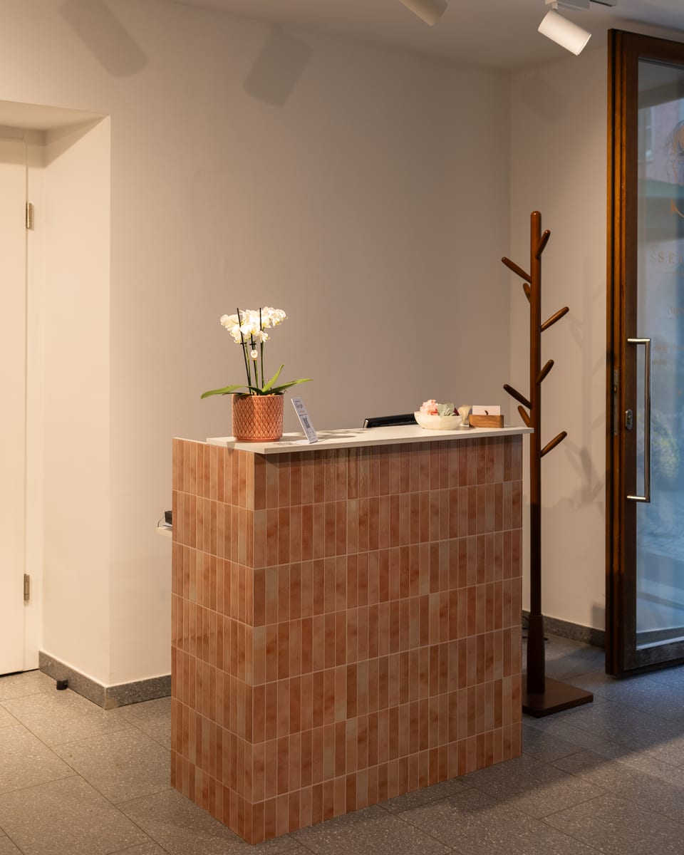Die geflieste Empfangstheke mit einer Orchidee, daneben die Garderobe und die Eingangstür