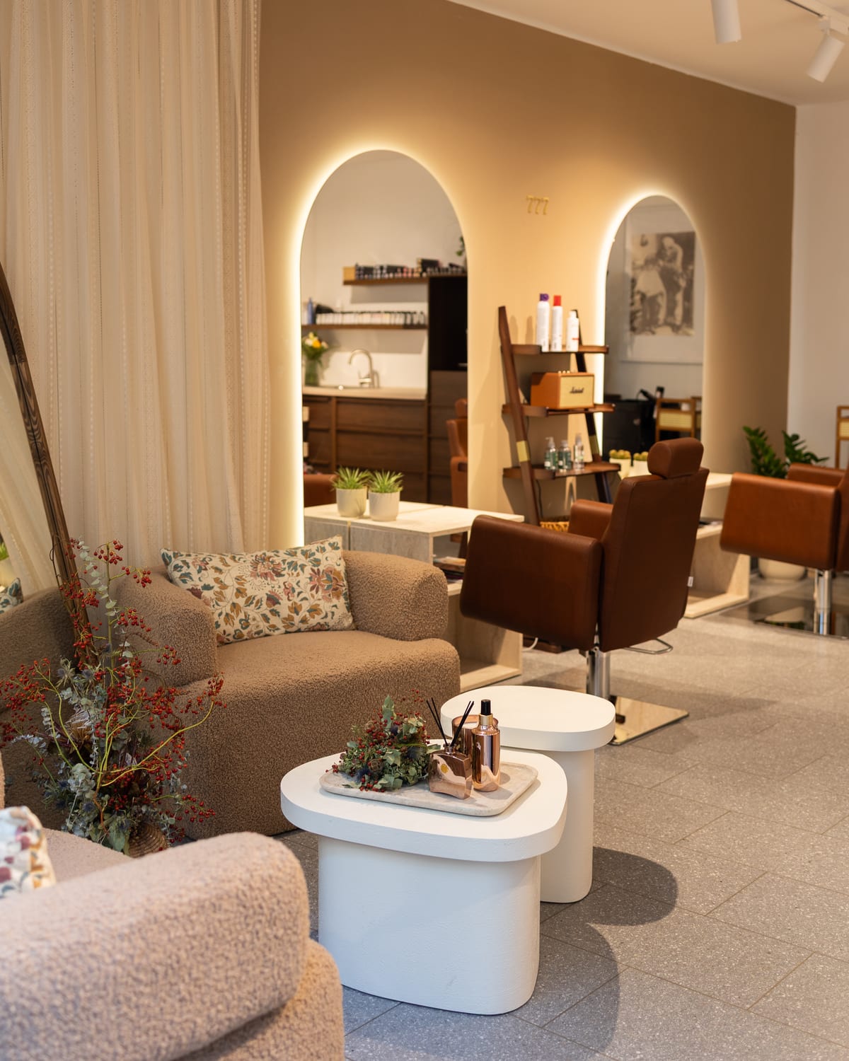 Der Salon: vorne zwei Sessel und kleine weiße Tische, dahinter die Wand mit zwei beleuchteten Bögen und den Friseurstühlen